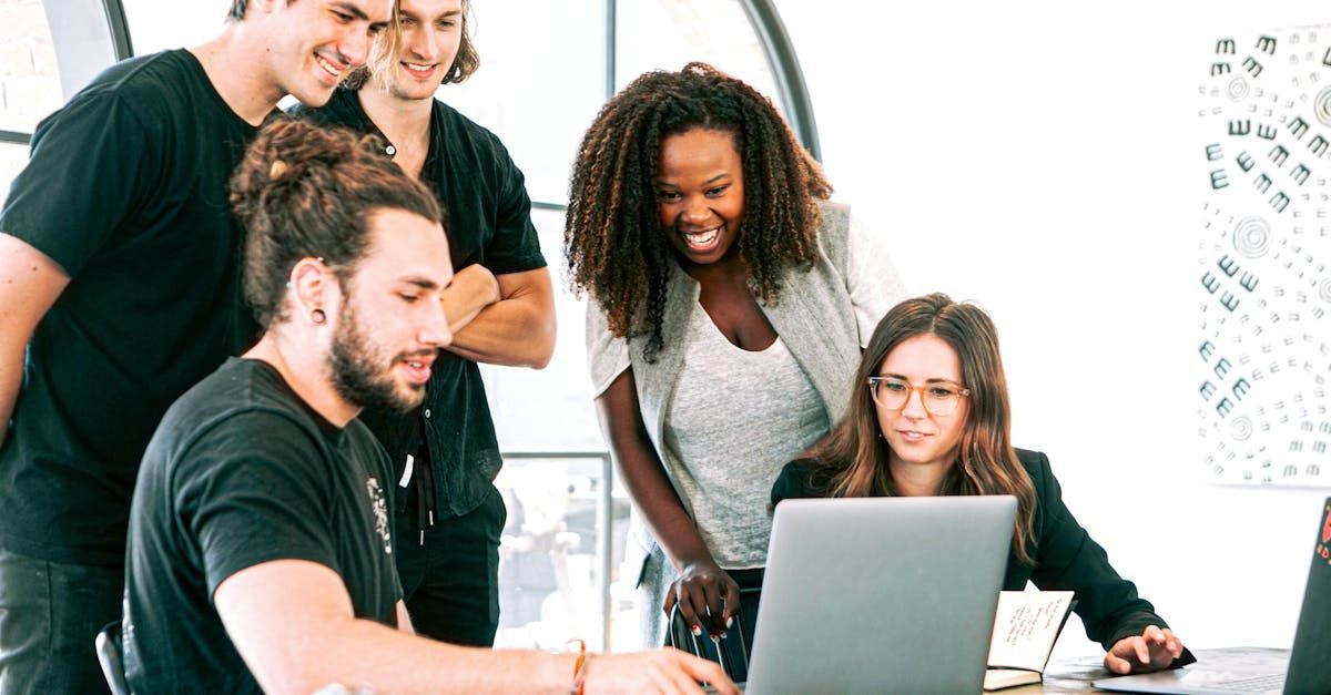 A group of people are standing around a laptop computer.