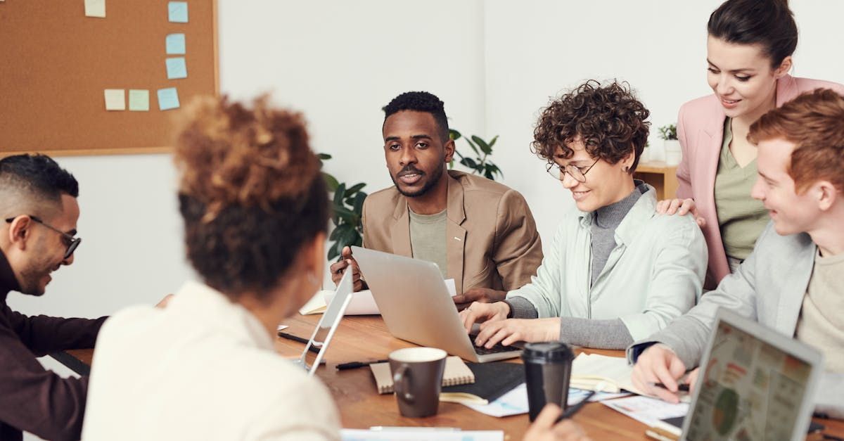 A group of people are sitting around a table with laptops.