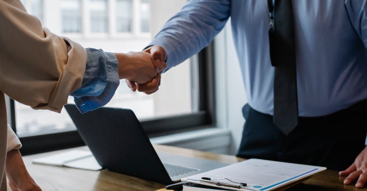 A man and a woman are shaking hands in front of a laptop.