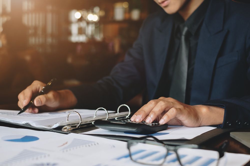 A man is sitting at a table using a calculator and a pen.