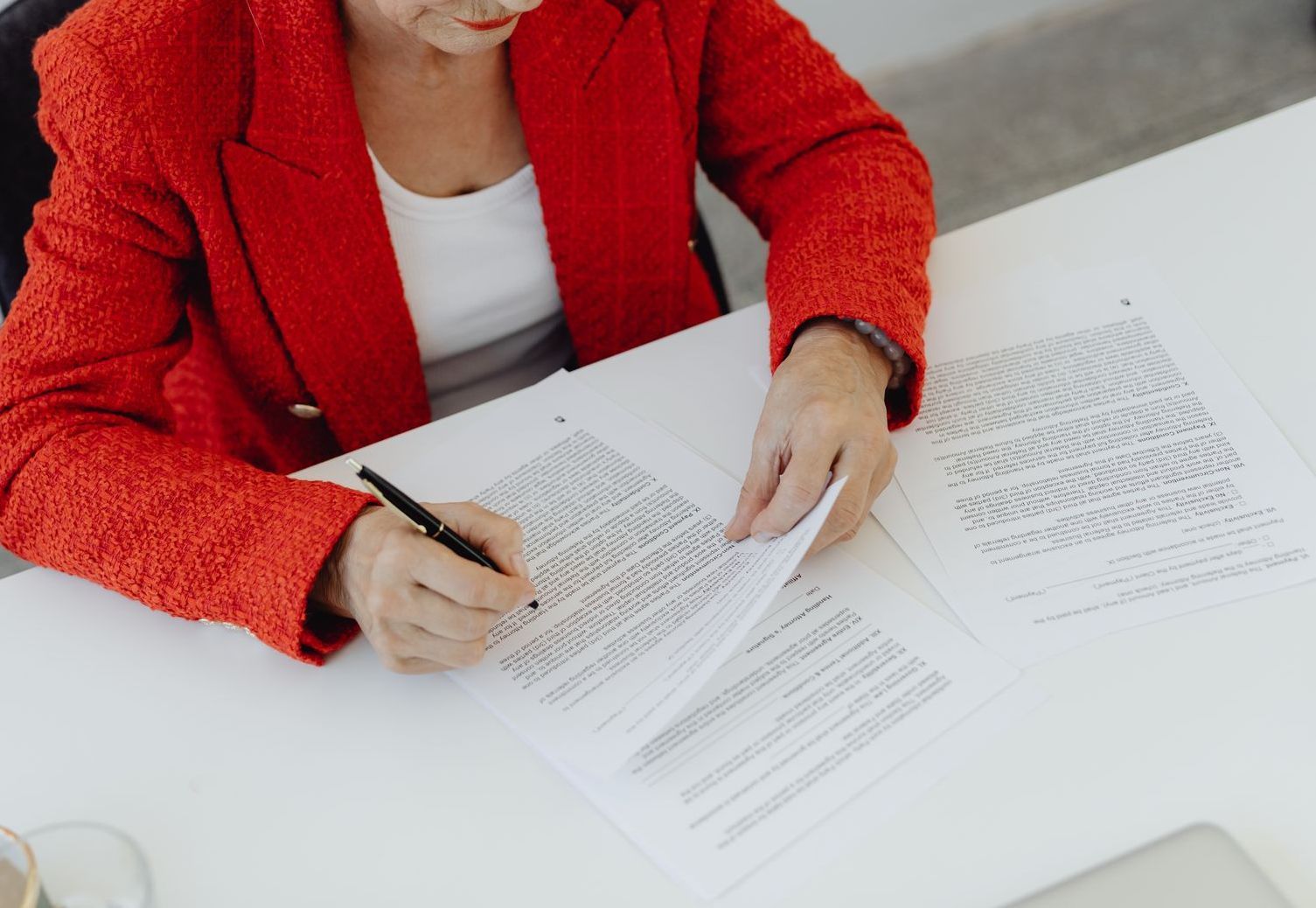 A woman in a red jacket is sitting at a table writing on a piece of paper.
