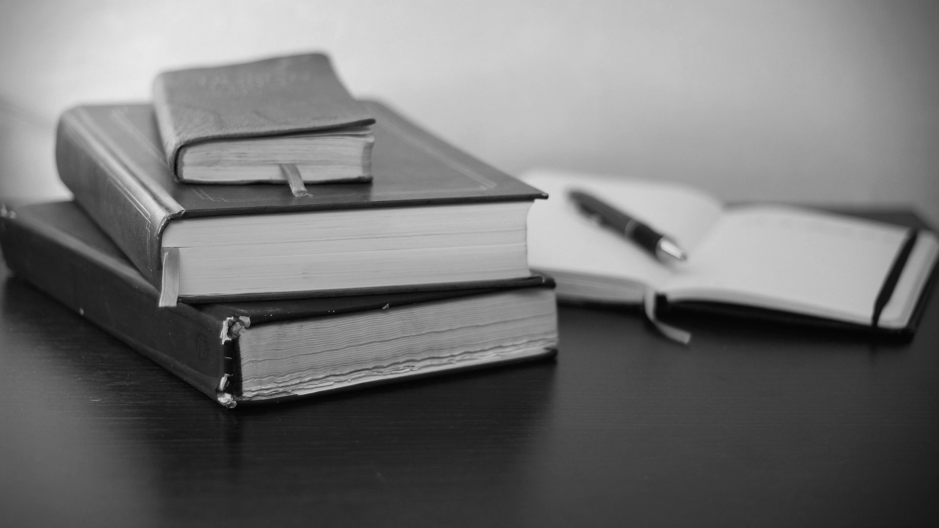 A black and white photo of three books stacked on top of each other on a table.