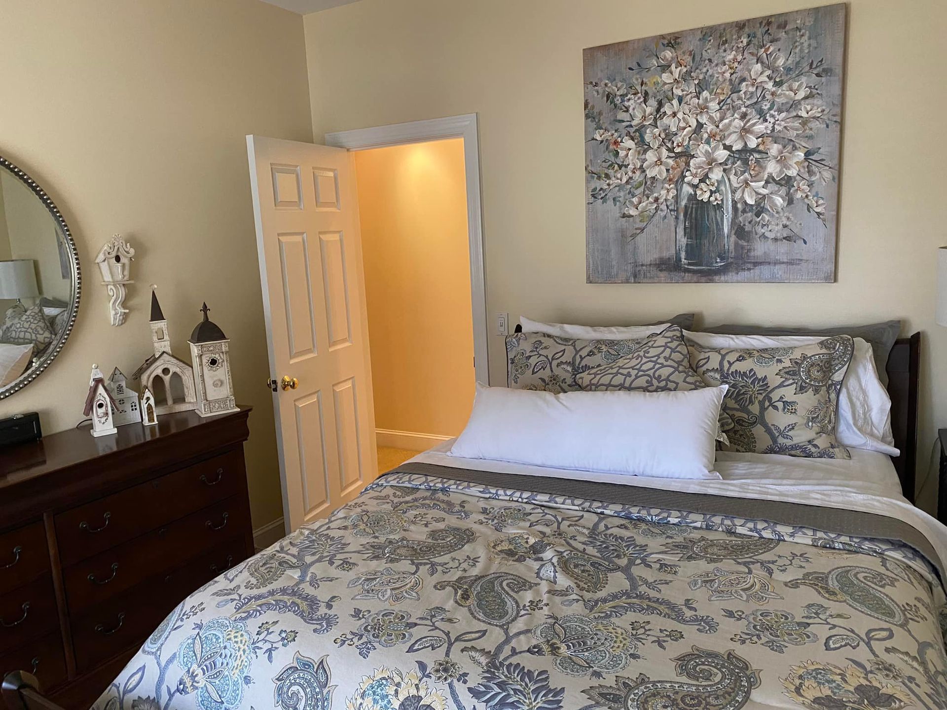 A bedroom with a bed , dresser , mirror and painting on the wall.