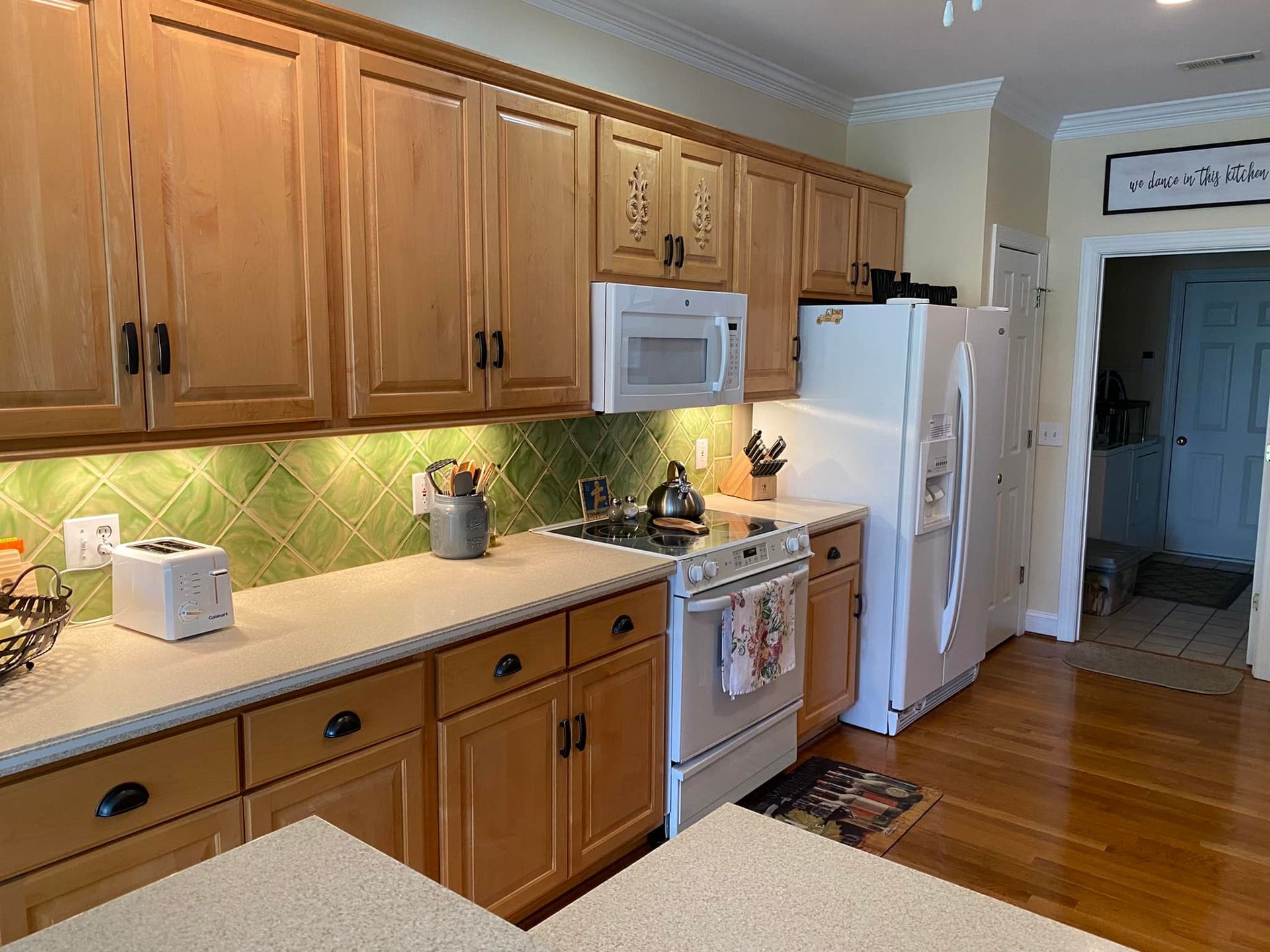 A kitchen with wooden cabinets , a stove , refrigerator , microwave and toaster oven.