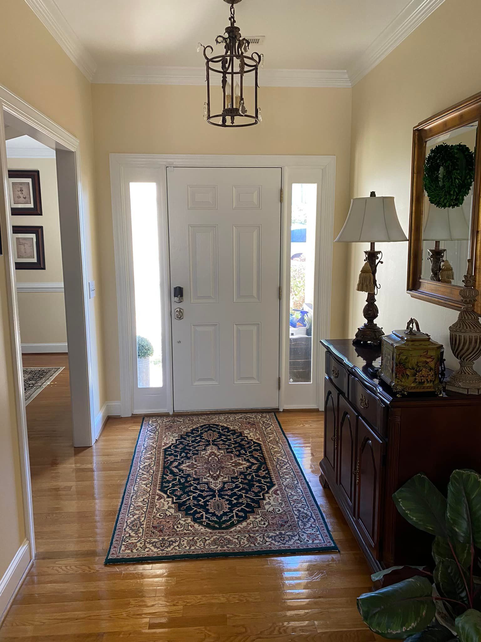 A hallway with a rug , lamp , mirror and dresser.