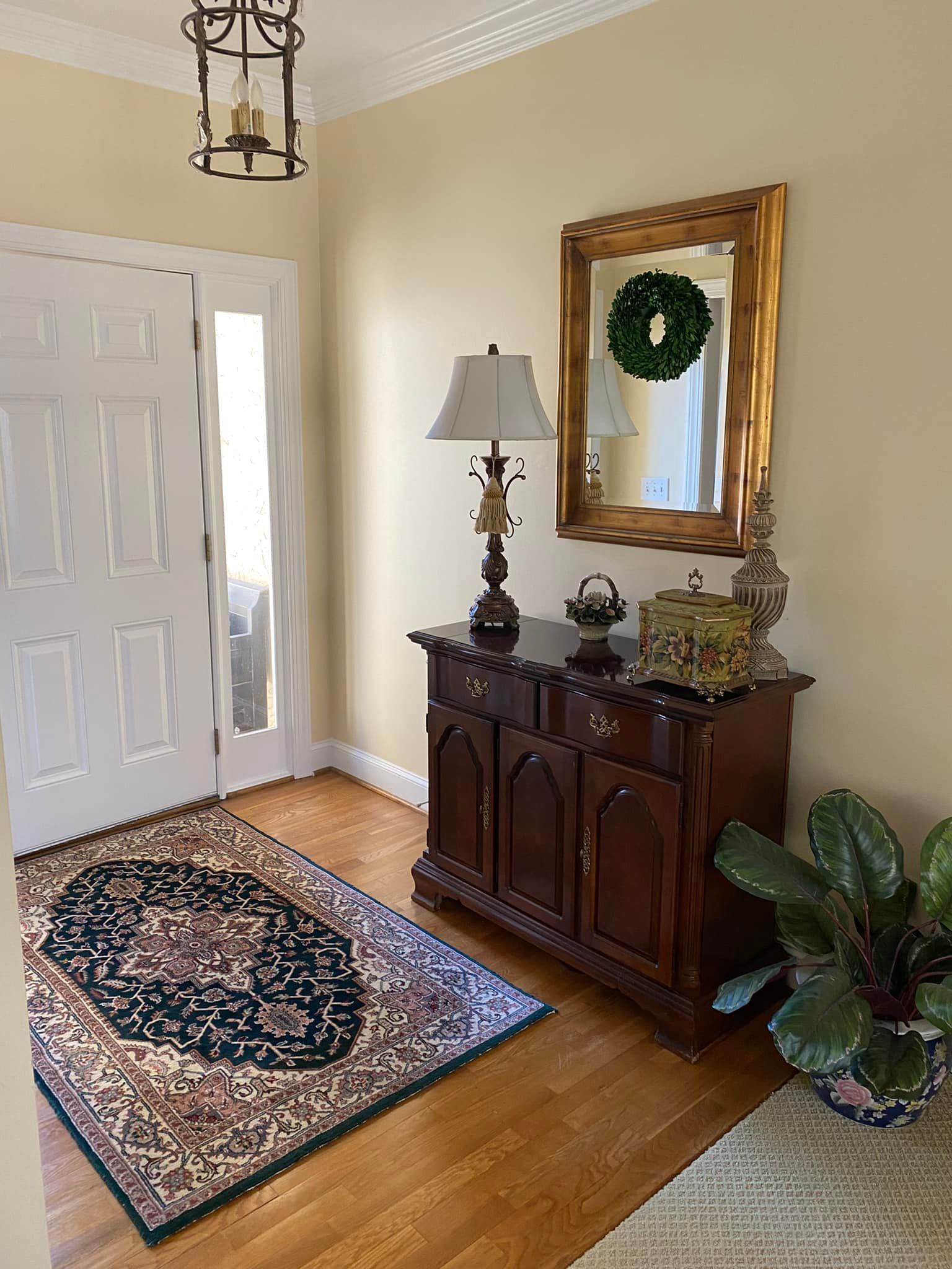 A hallway with a dresser , lamp , mirror and rug.