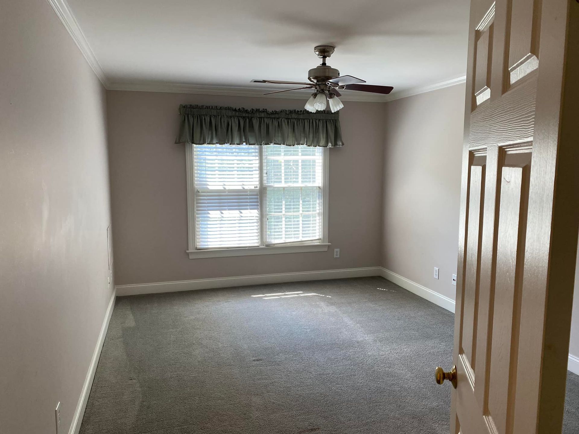 An empty bedroom with a ceiling fan and a window.