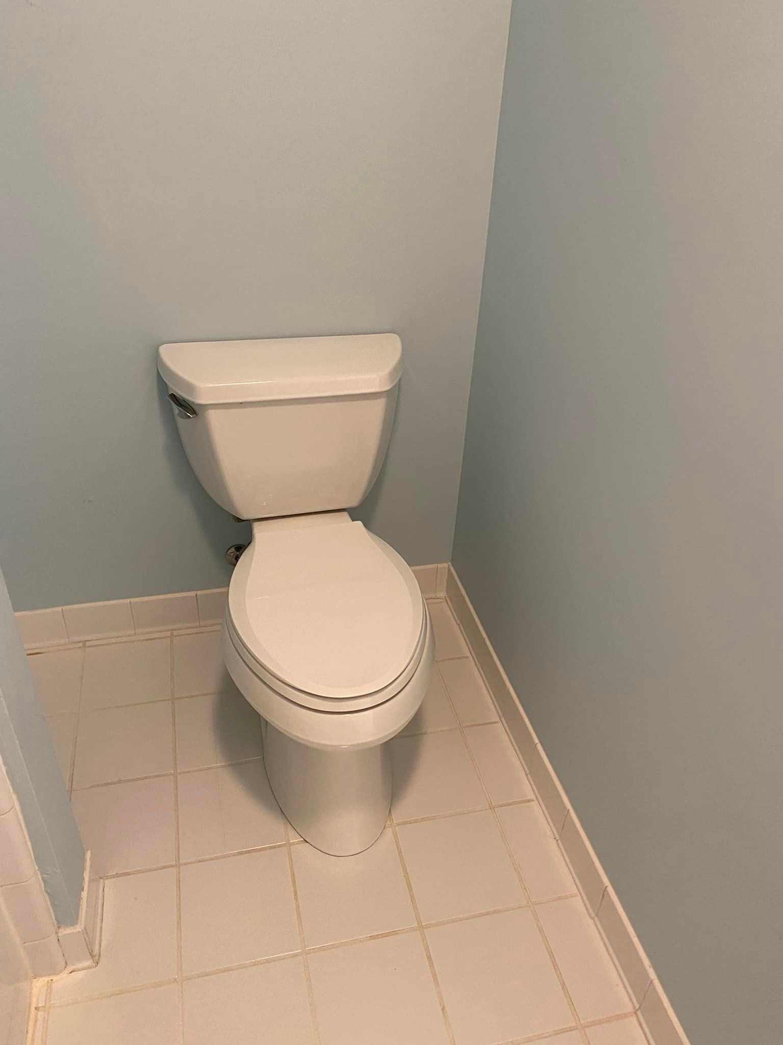 A white toilet is sitting in a corner of a bathroom.