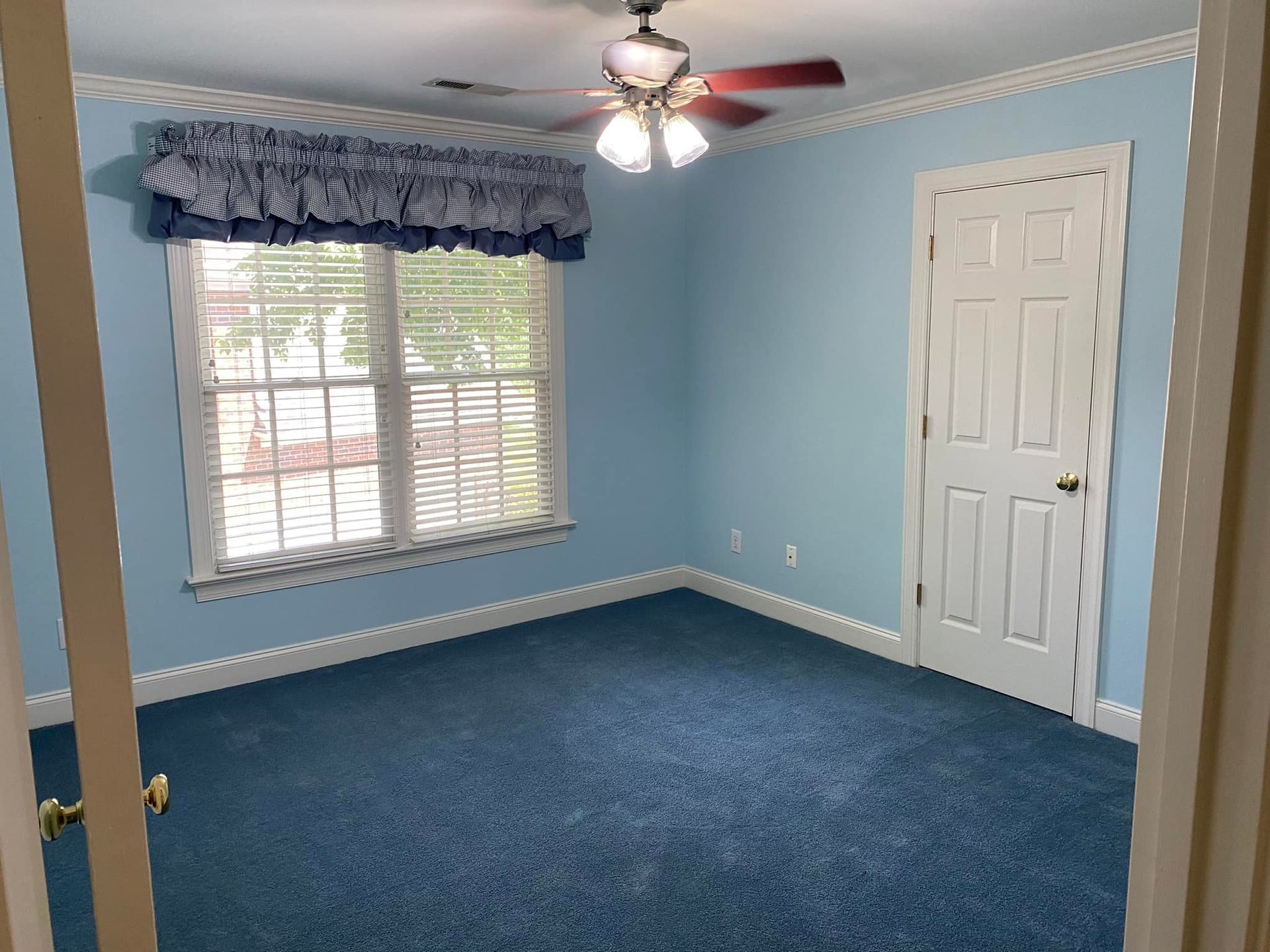 An empty bedroom with blue carpet and a ceiling fan.