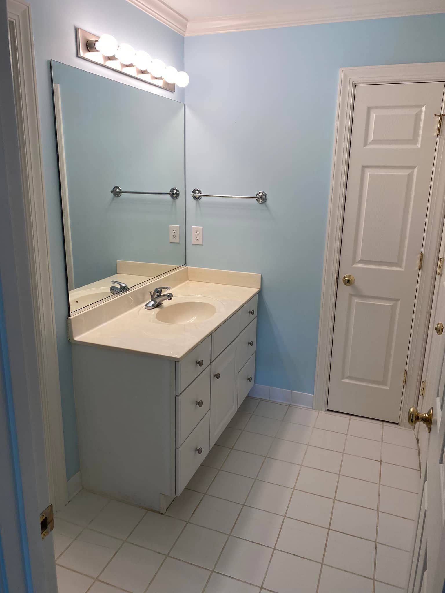 A bathroom with a sink , mirror , and door.