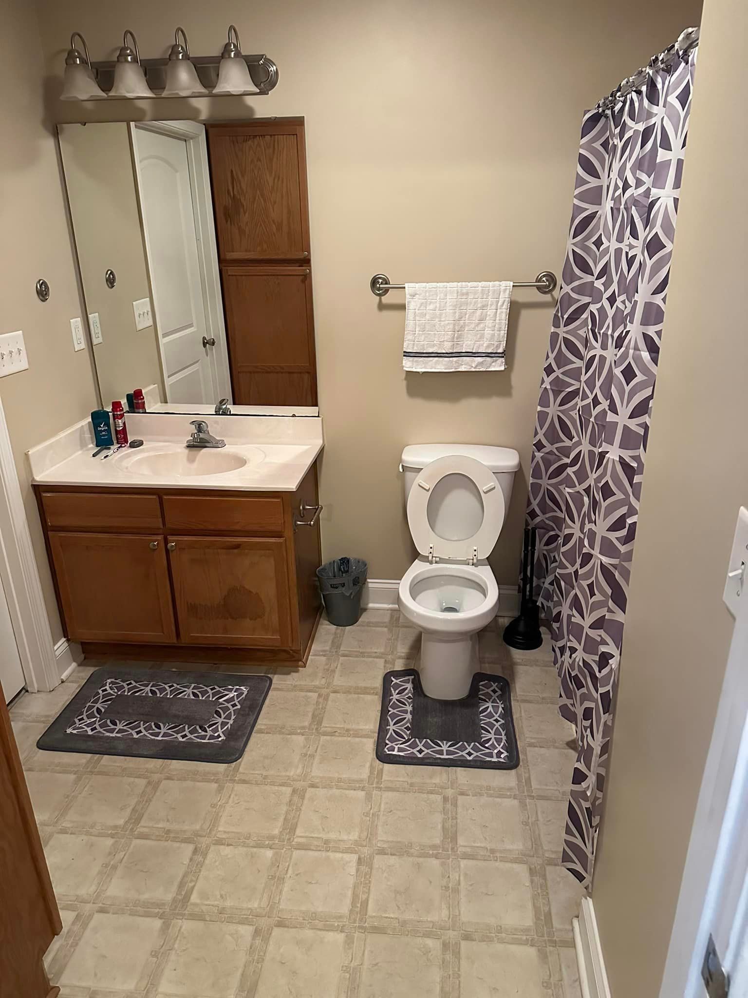 A bathroom with a toilet , sink , mirror and shower curtain.