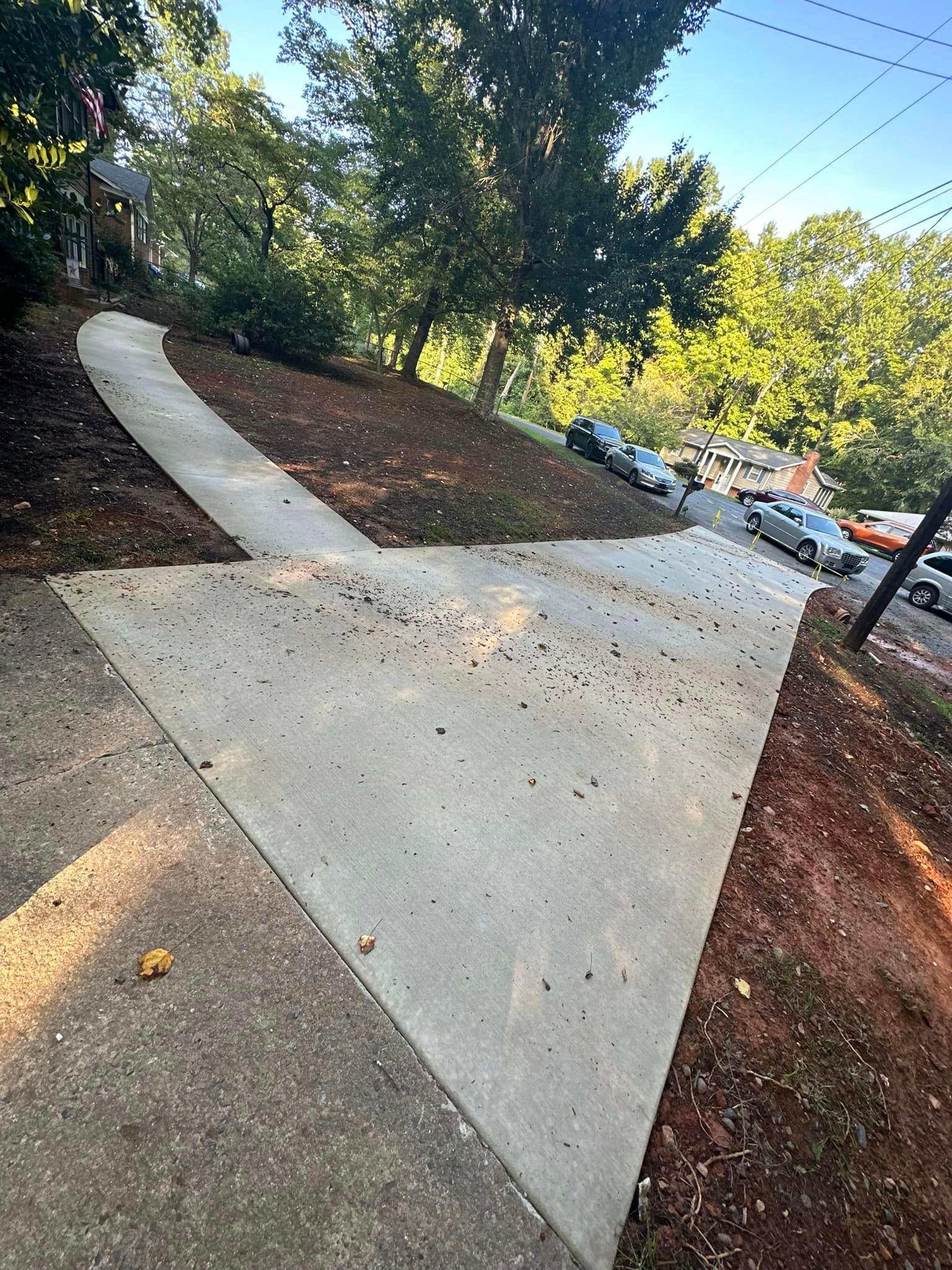 A concrete walkway going up a hill with cars parked on the side of it.
