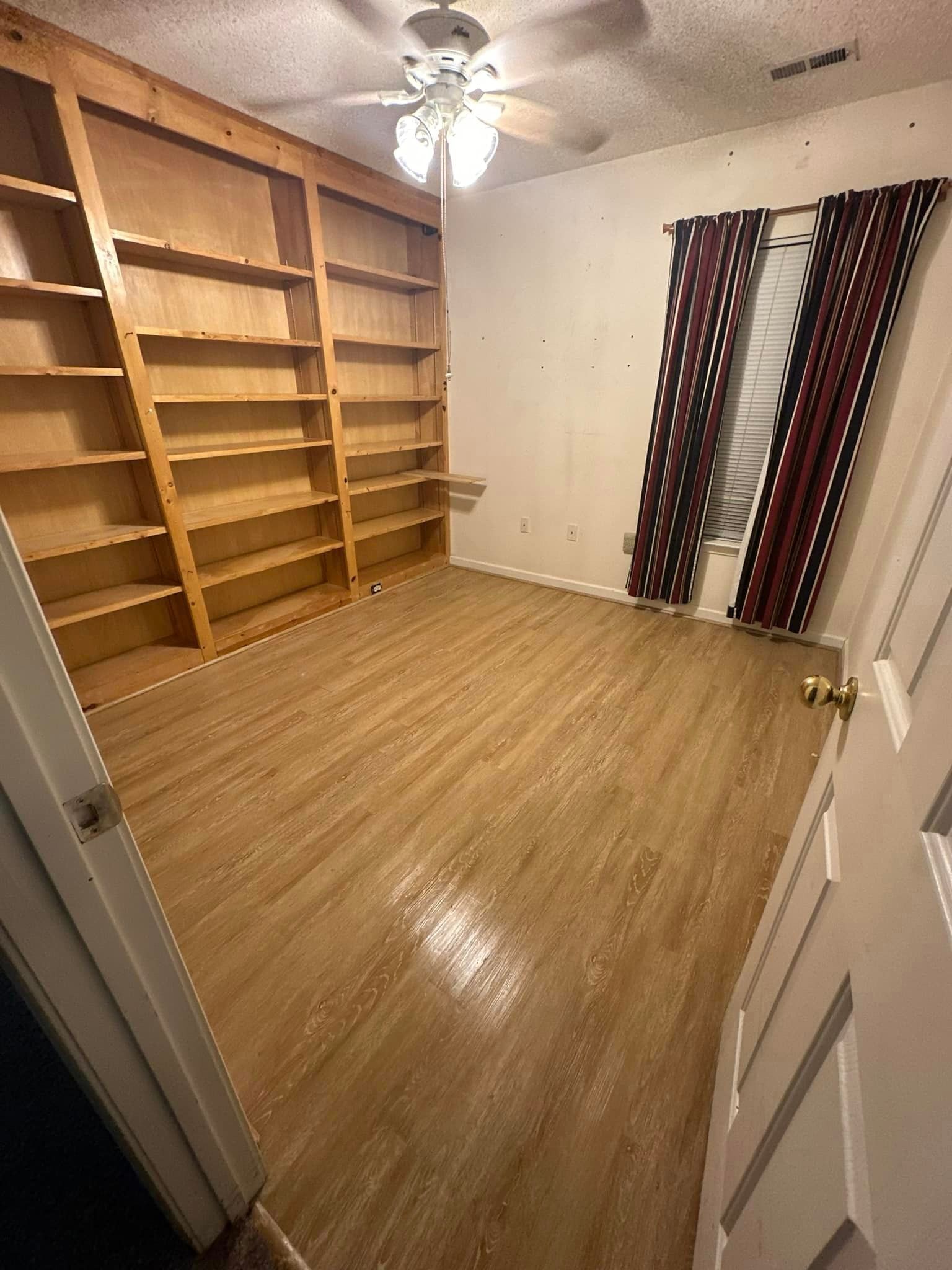 A room with a lot of shelves and a ceiling fan.