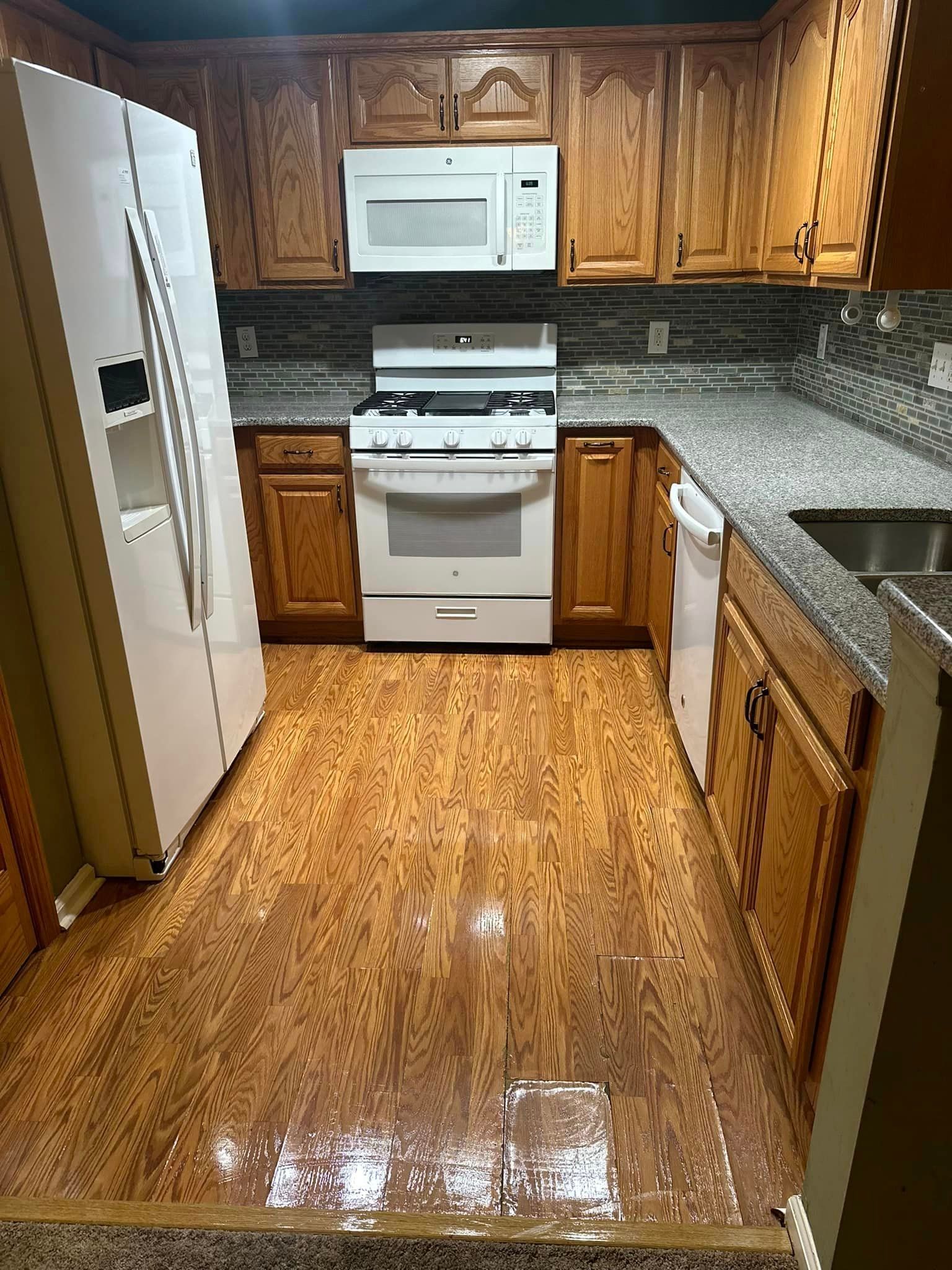 A kitchen with a stove , refrigerator , microwave and sink.