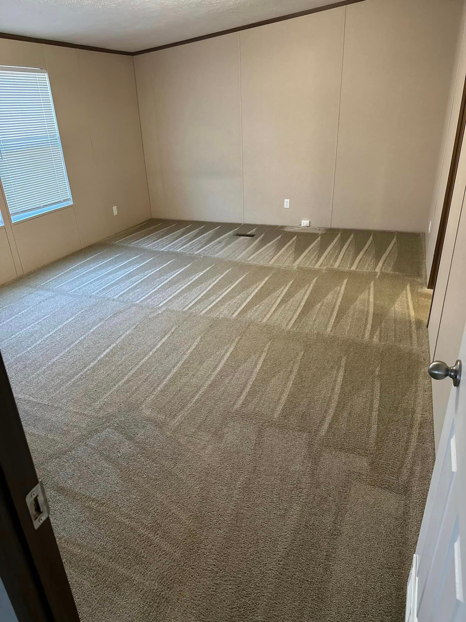 An empty room with a carpeted floor and a window.