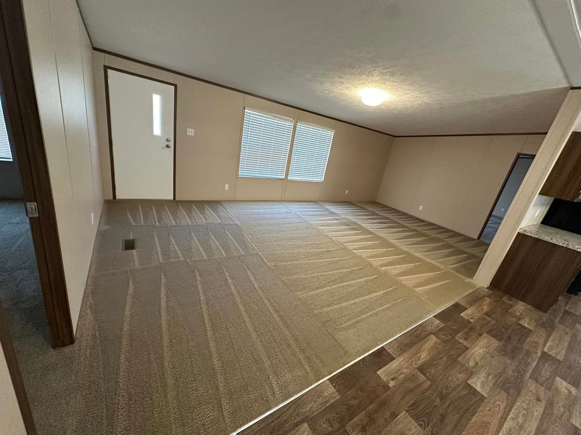 A living room in a mobile home with a carpeted floor and wooden floors.
