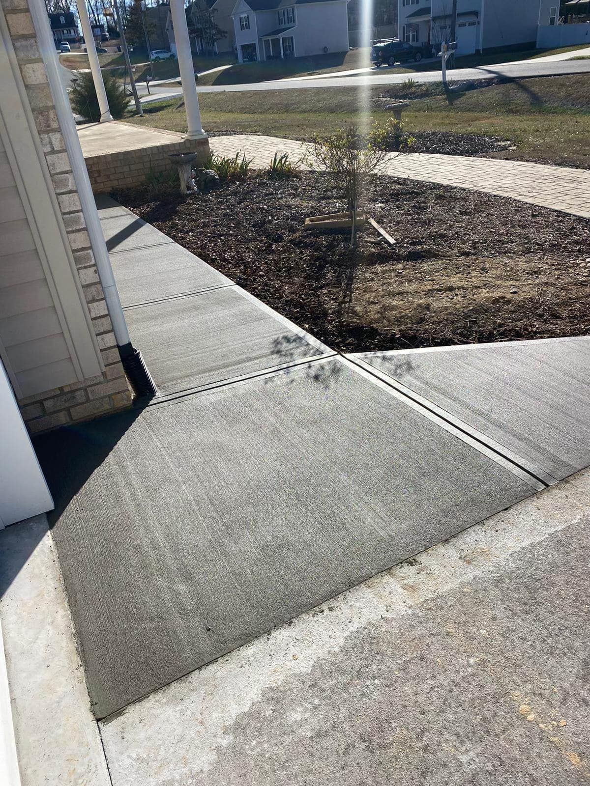 A concrete walkway leading to a house with a tree in the background.