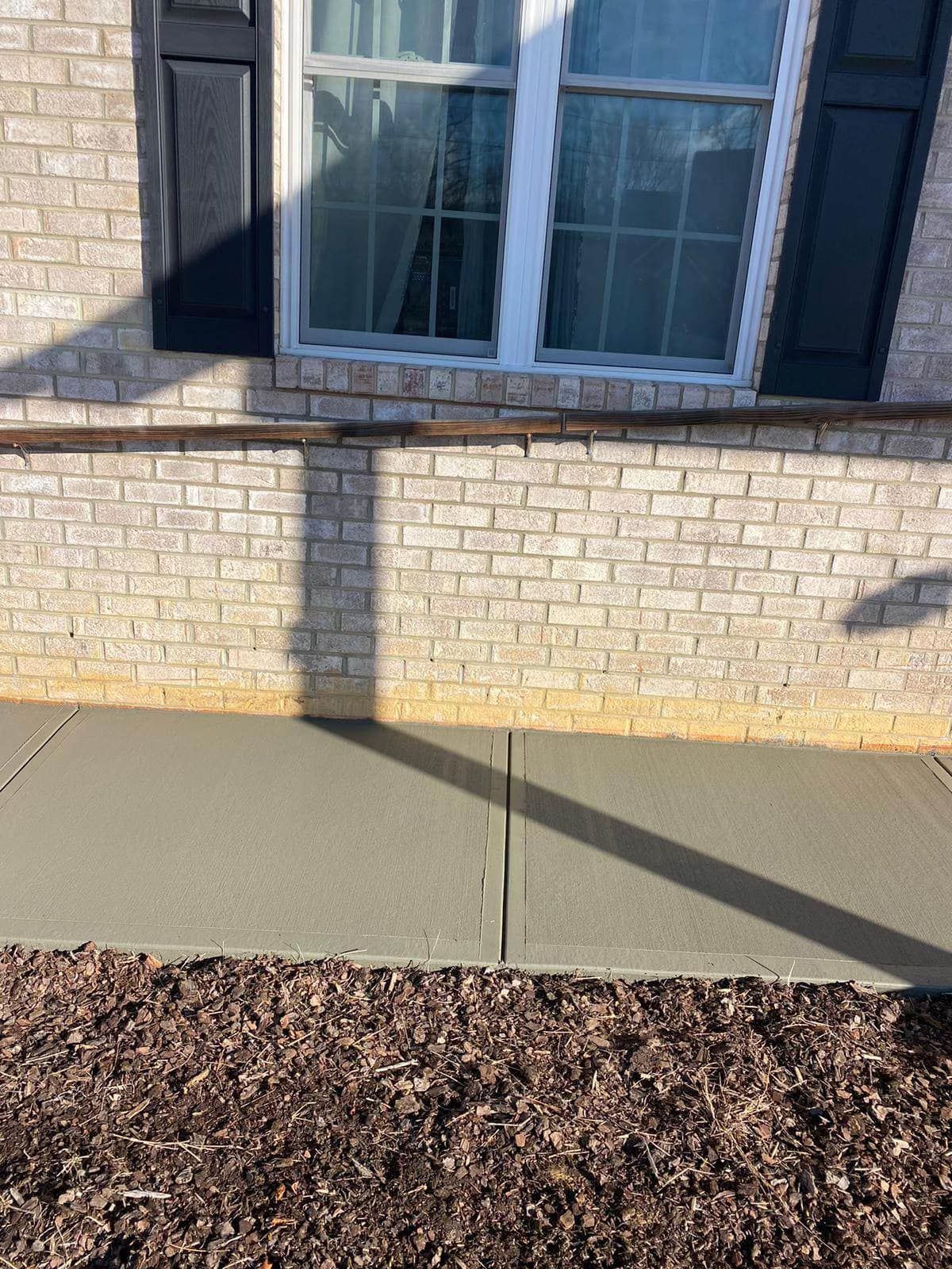 A brick wall with a window and a sidewalk in front of it.
