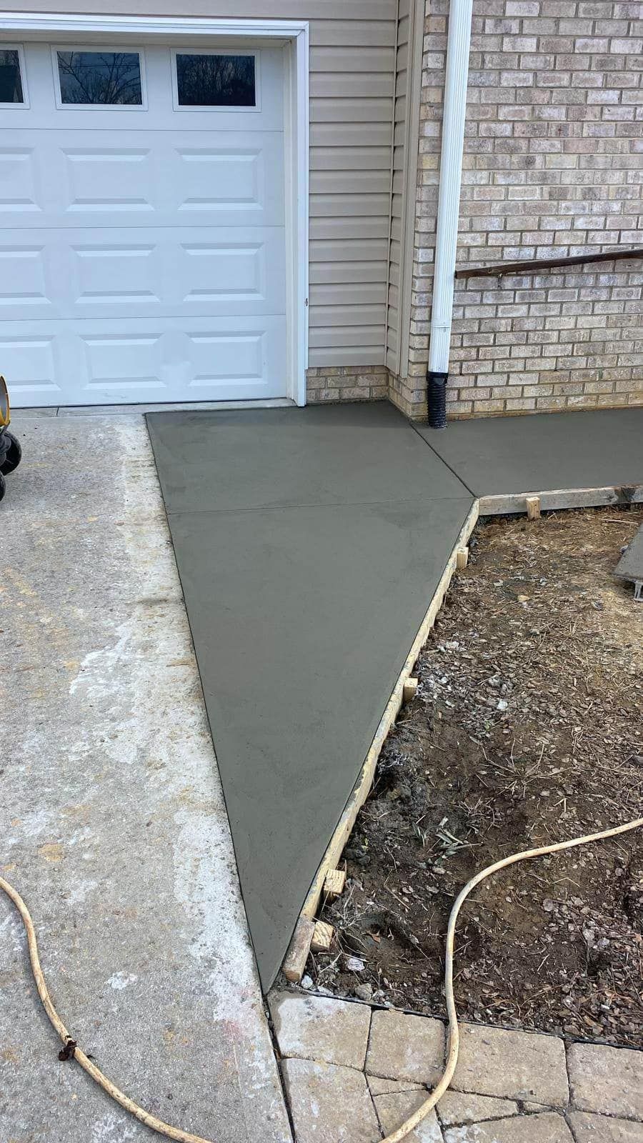 A concrete walkway is being built next to a garage door.