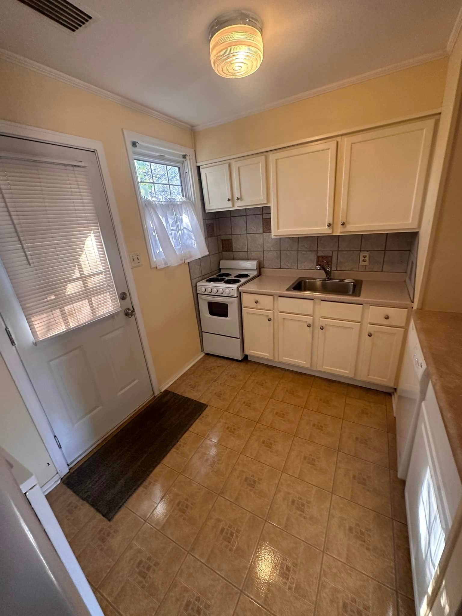 A kitchen with white cabinets , a stove , a sink , and a door.
