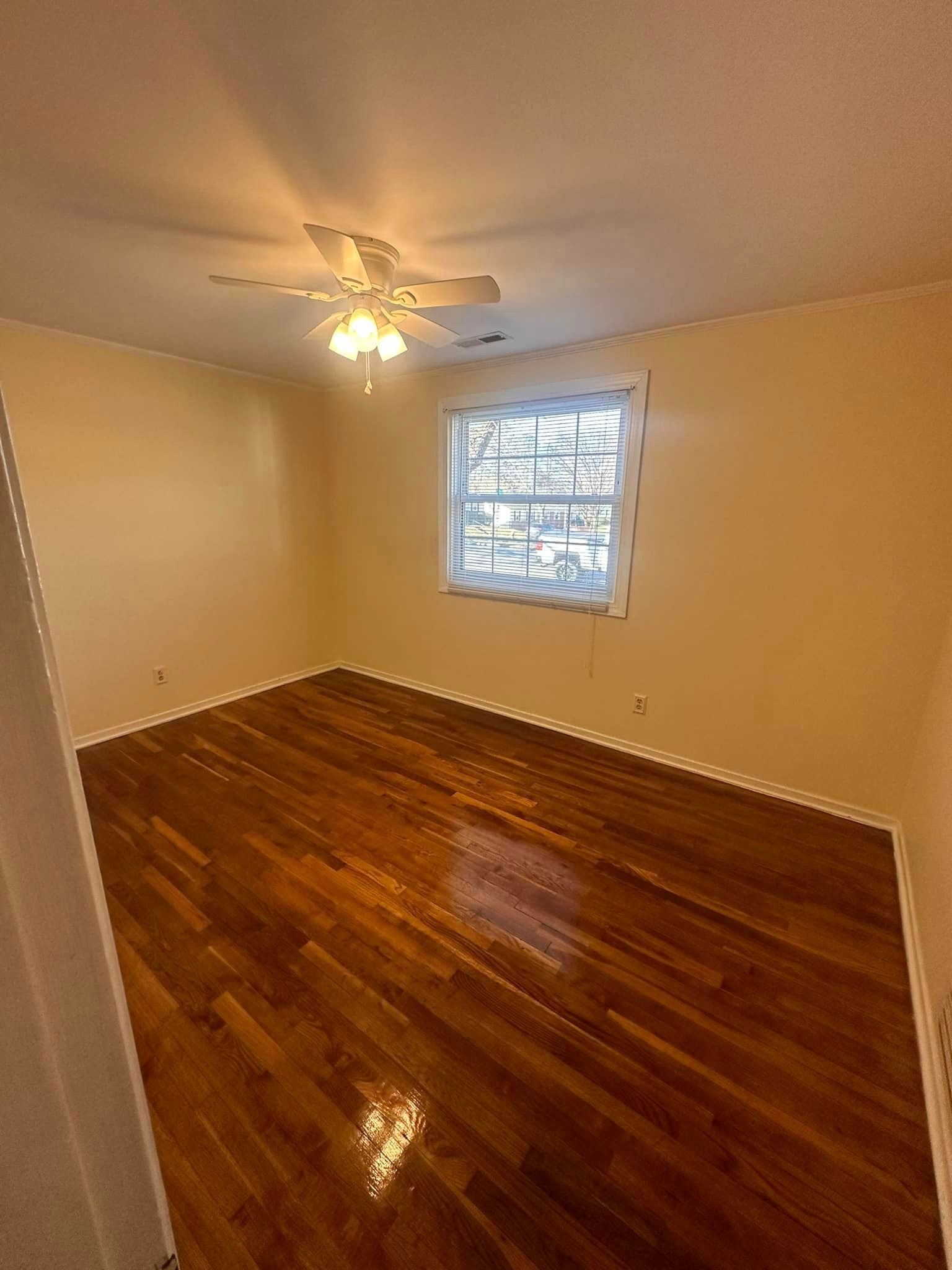 An empty room with hardwood floors and a ceiling fan.