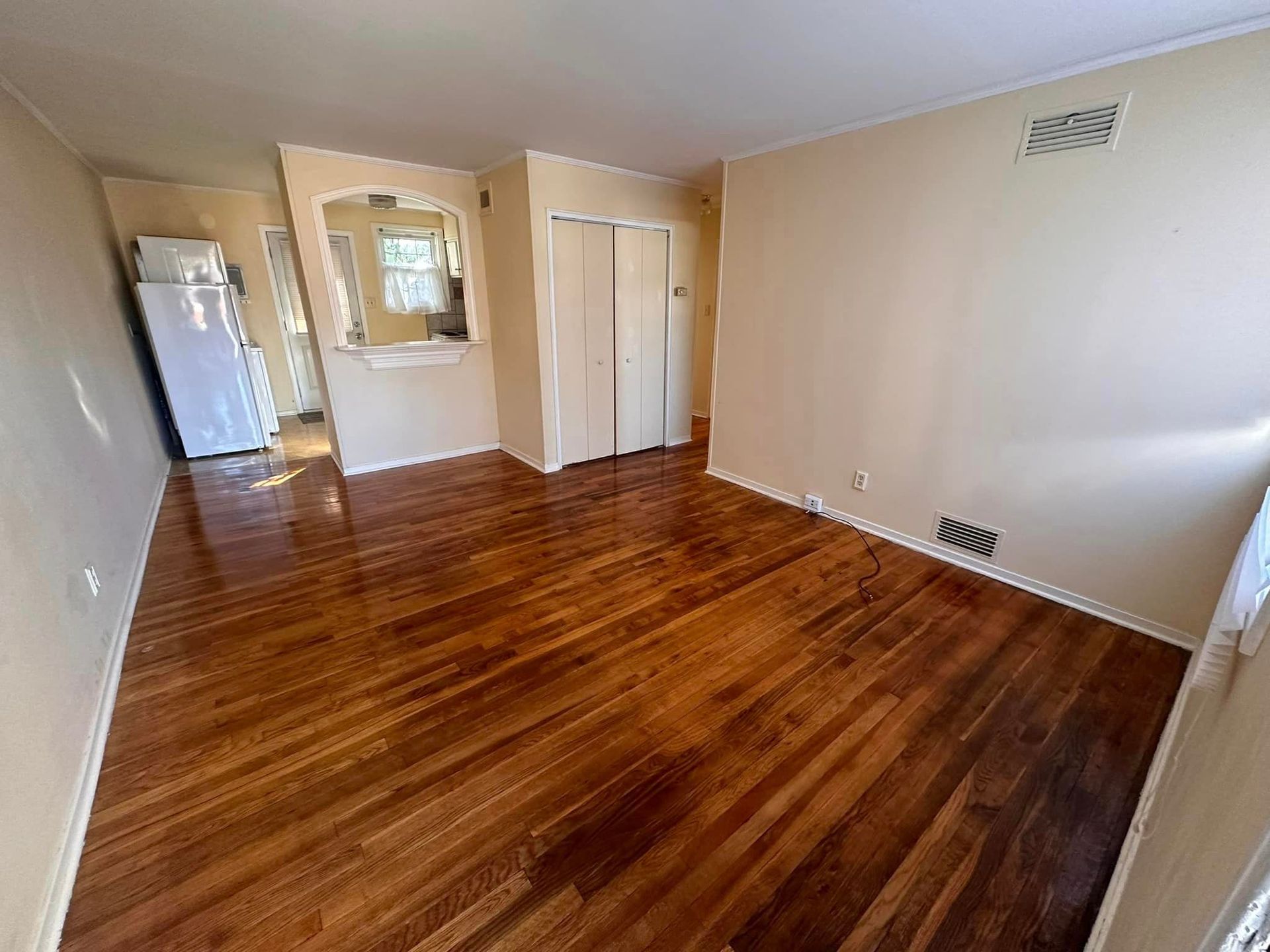 A living room with hardwood floors and a refrigerator.