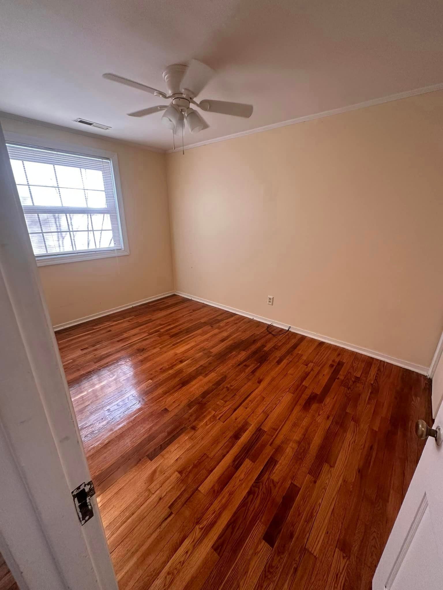 An empty bedroom with hardwood floors and a ceiling fan.