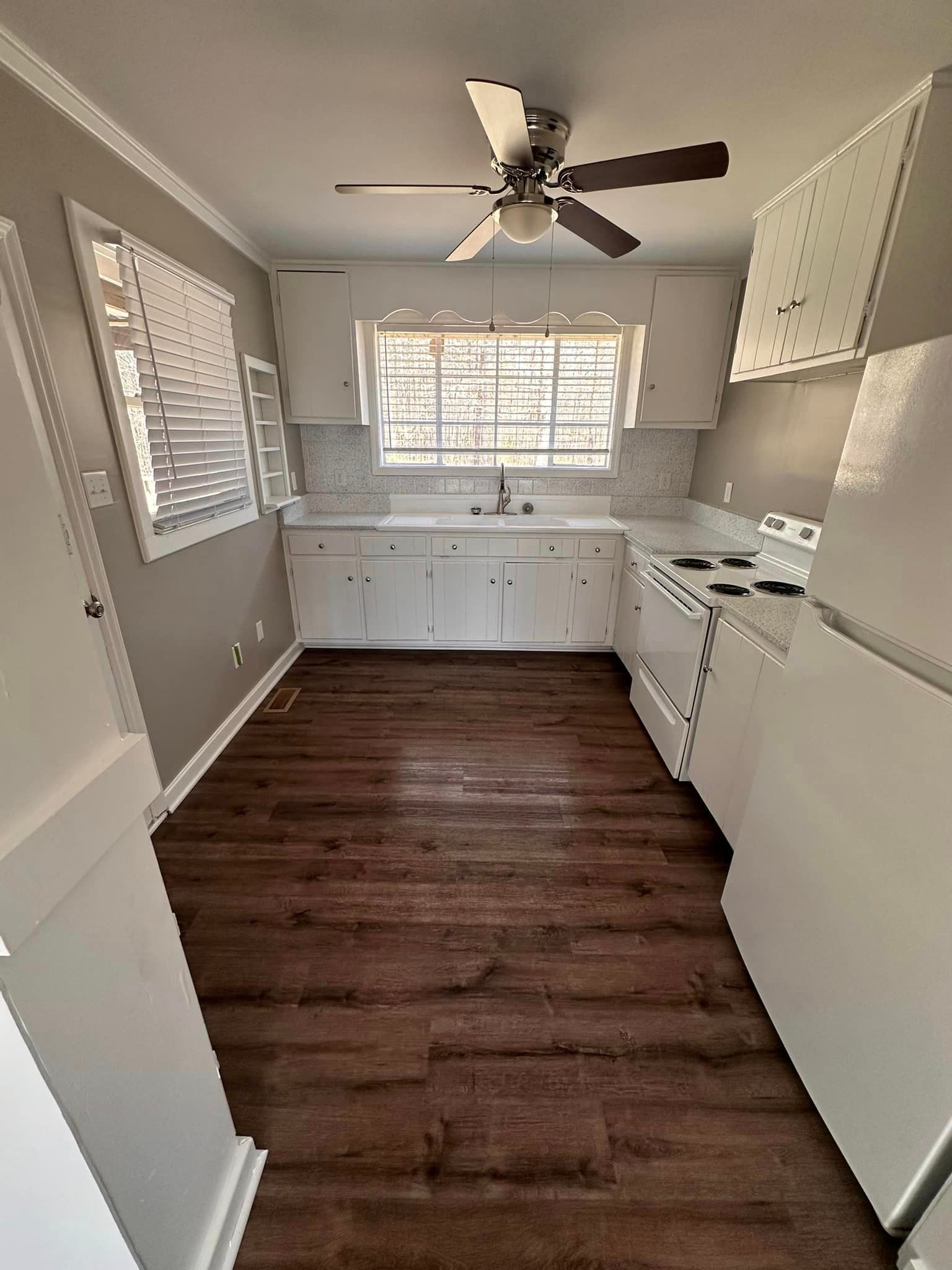 A kitchen with white cabinets , a stove , a refrigerator , and a ceiling fan.