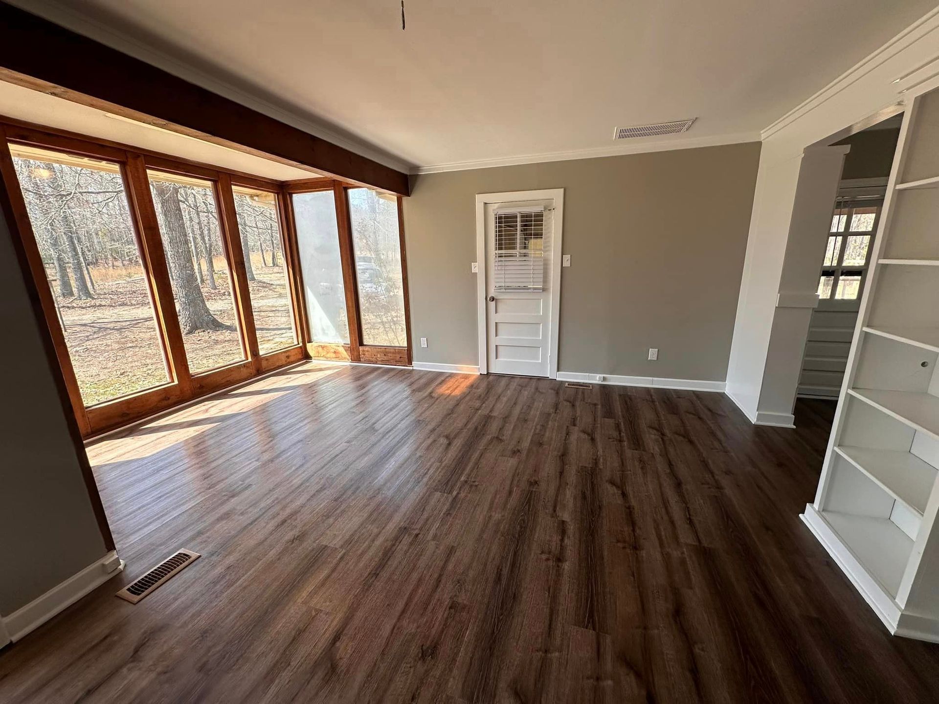An empty living room with hardwood floors and lots of windows.