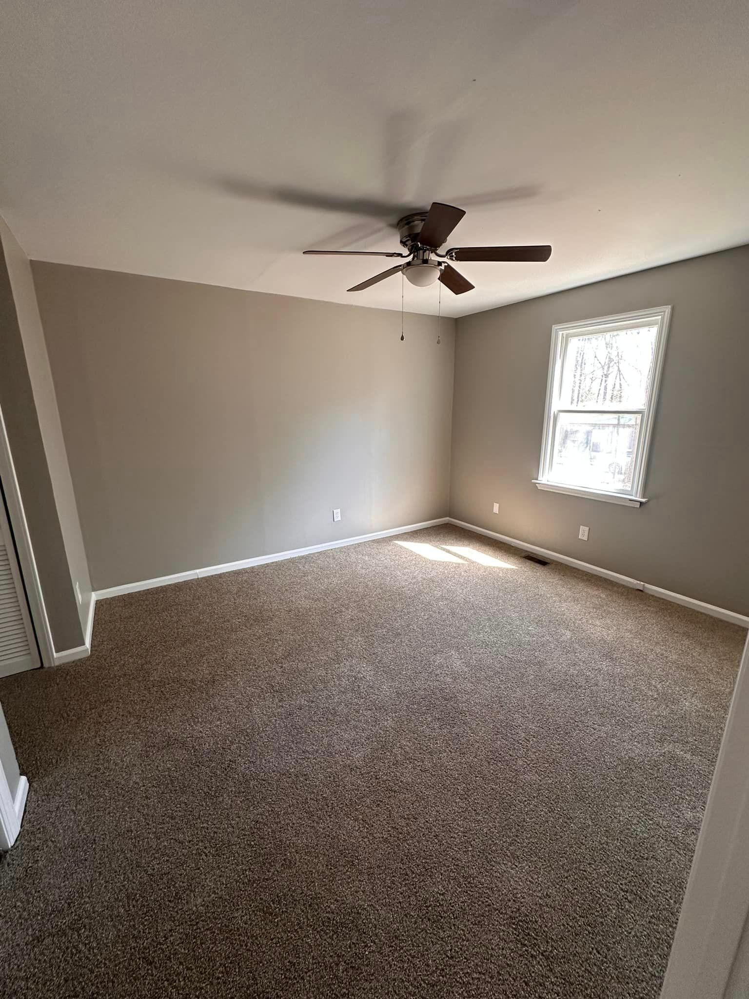 An empty room with a ceiling fan and a window.