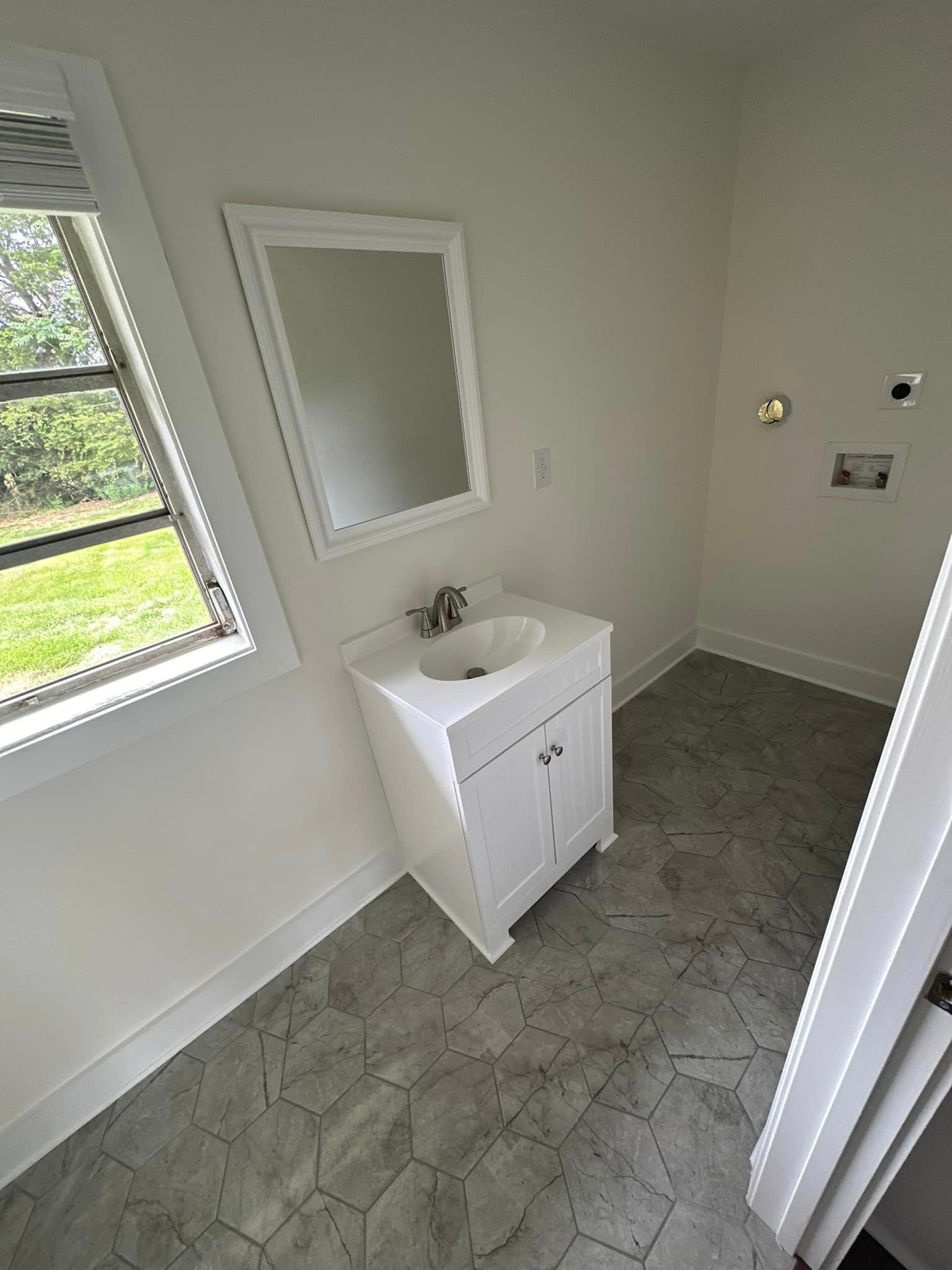 A bathroom with a sink , mirror and window.