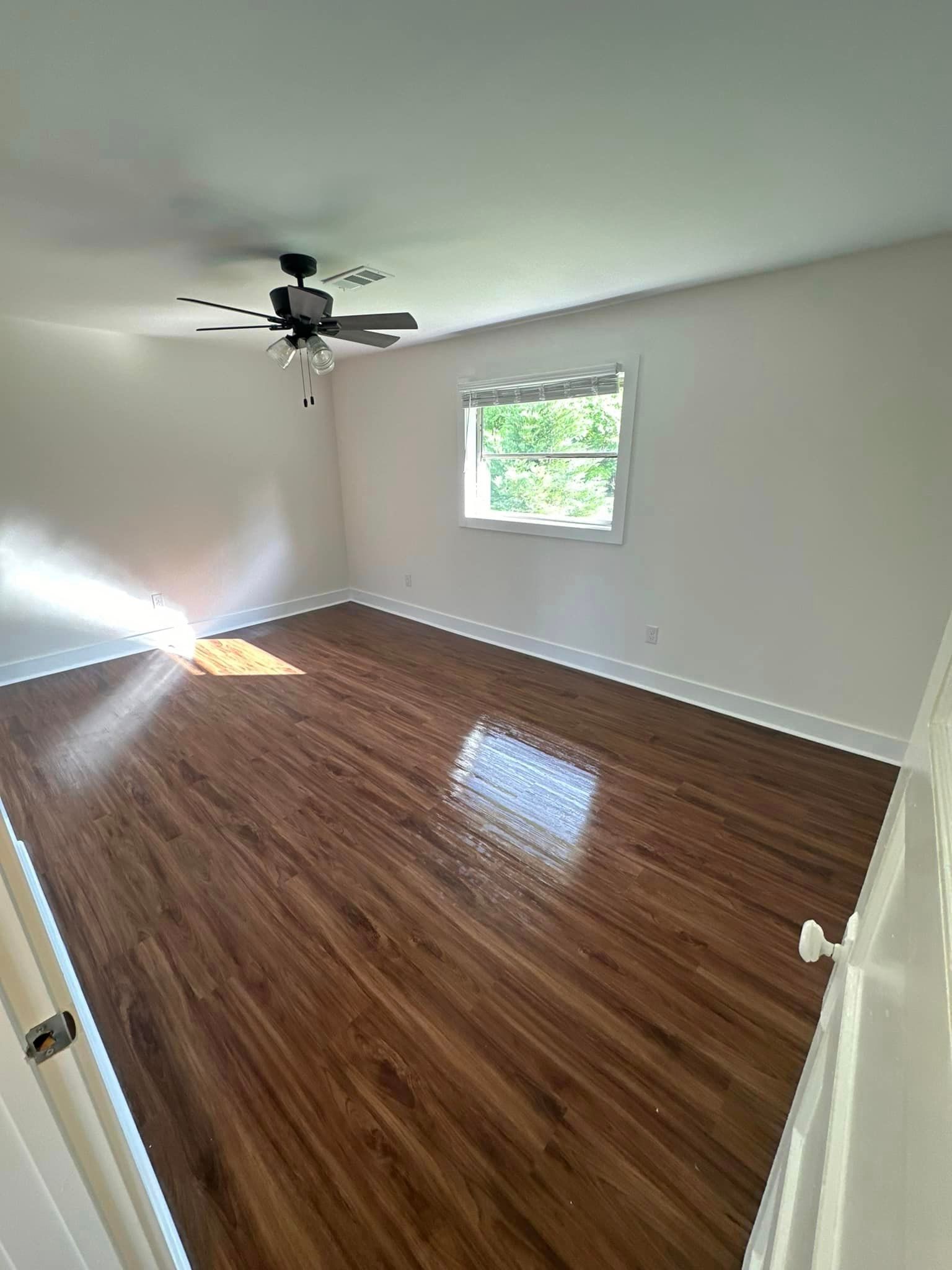 An empty room with hardwood floors and a ceiling fan.