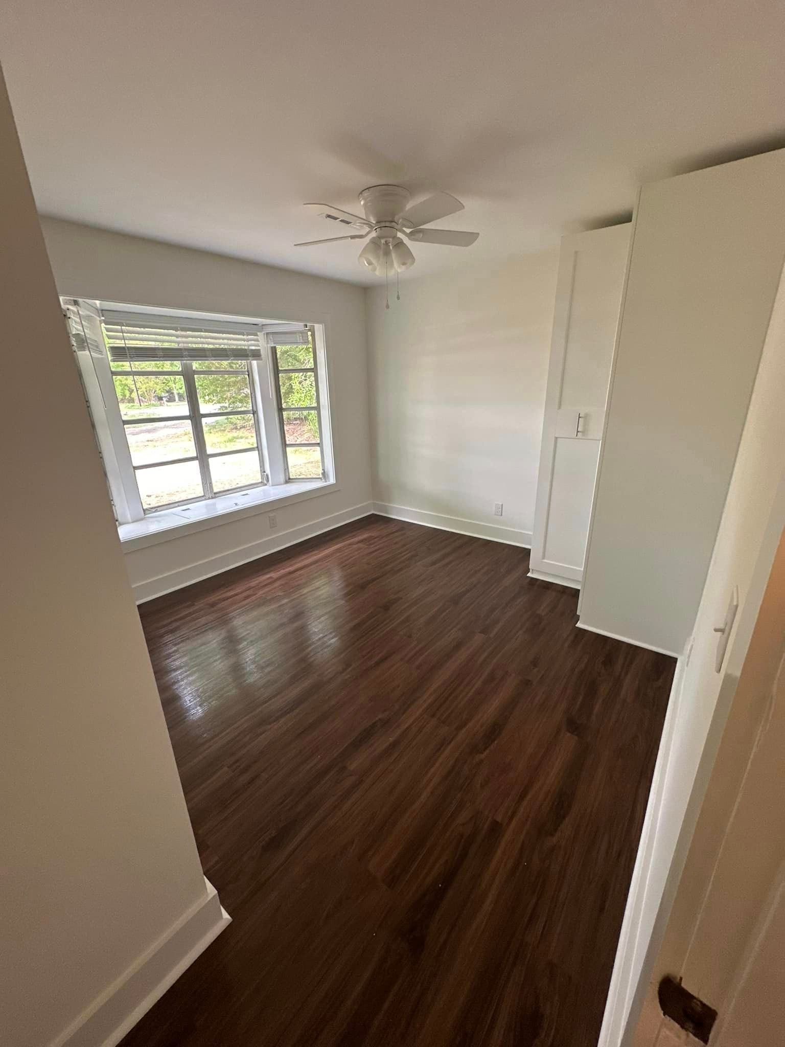 An empty bedroom with hardwood floors and a ceiling fan.