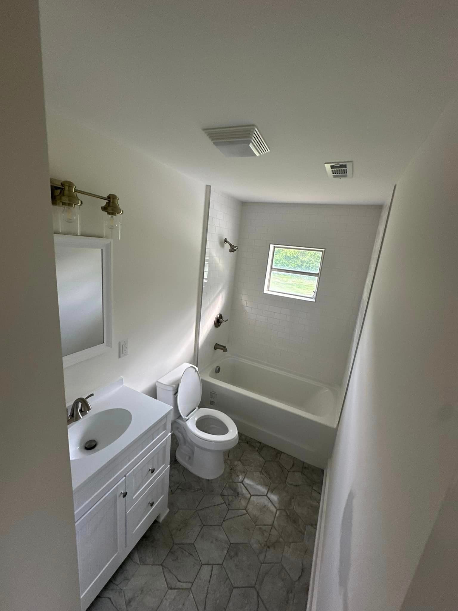 A bathroom with a toilet , sink , bathtub and window.