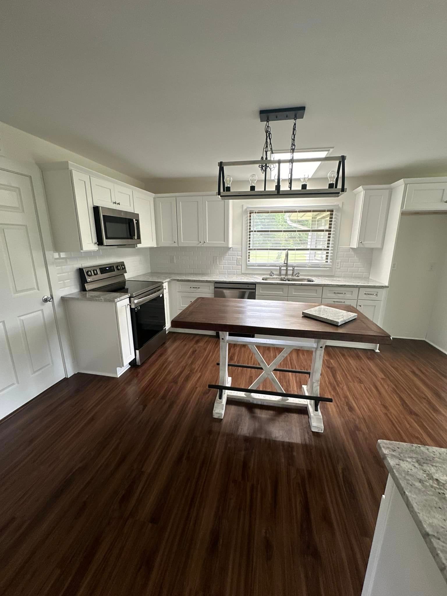 A kitchen with white cabinets , a wooden table , a stove , and a window.