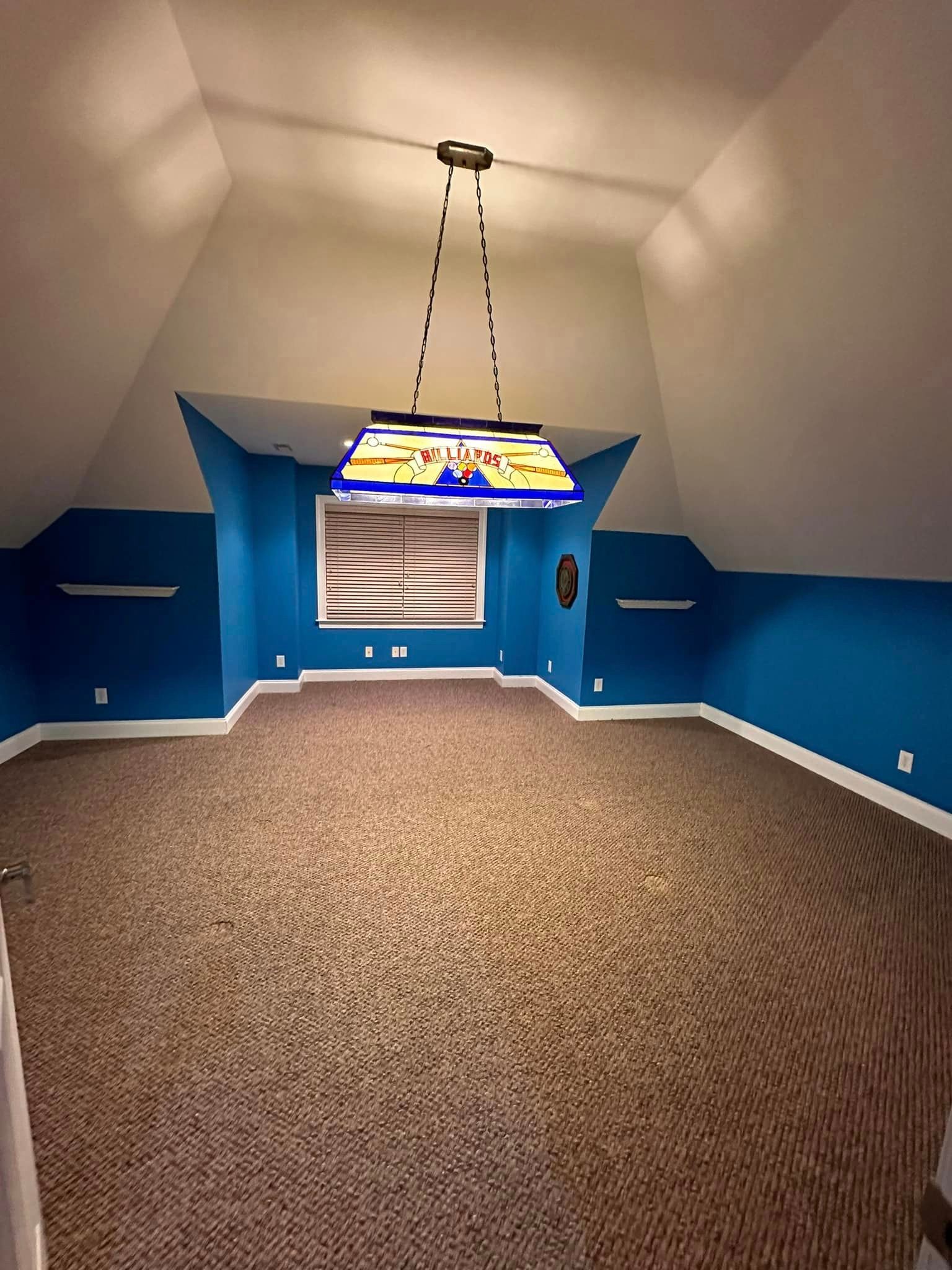 An empty room with blue walls and a pool table light hanging from the ceiling.