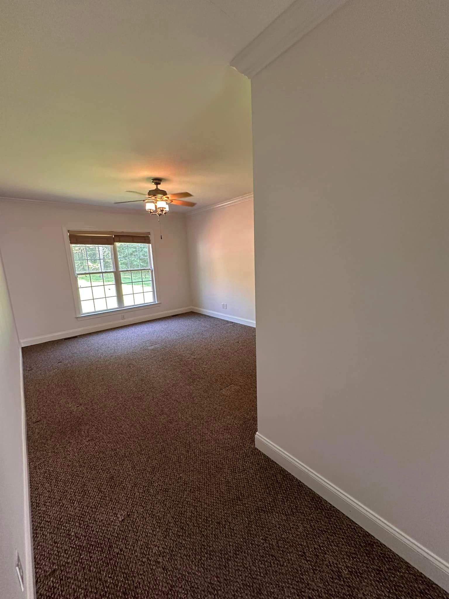 An empty room with a ceiling fan and two windows.