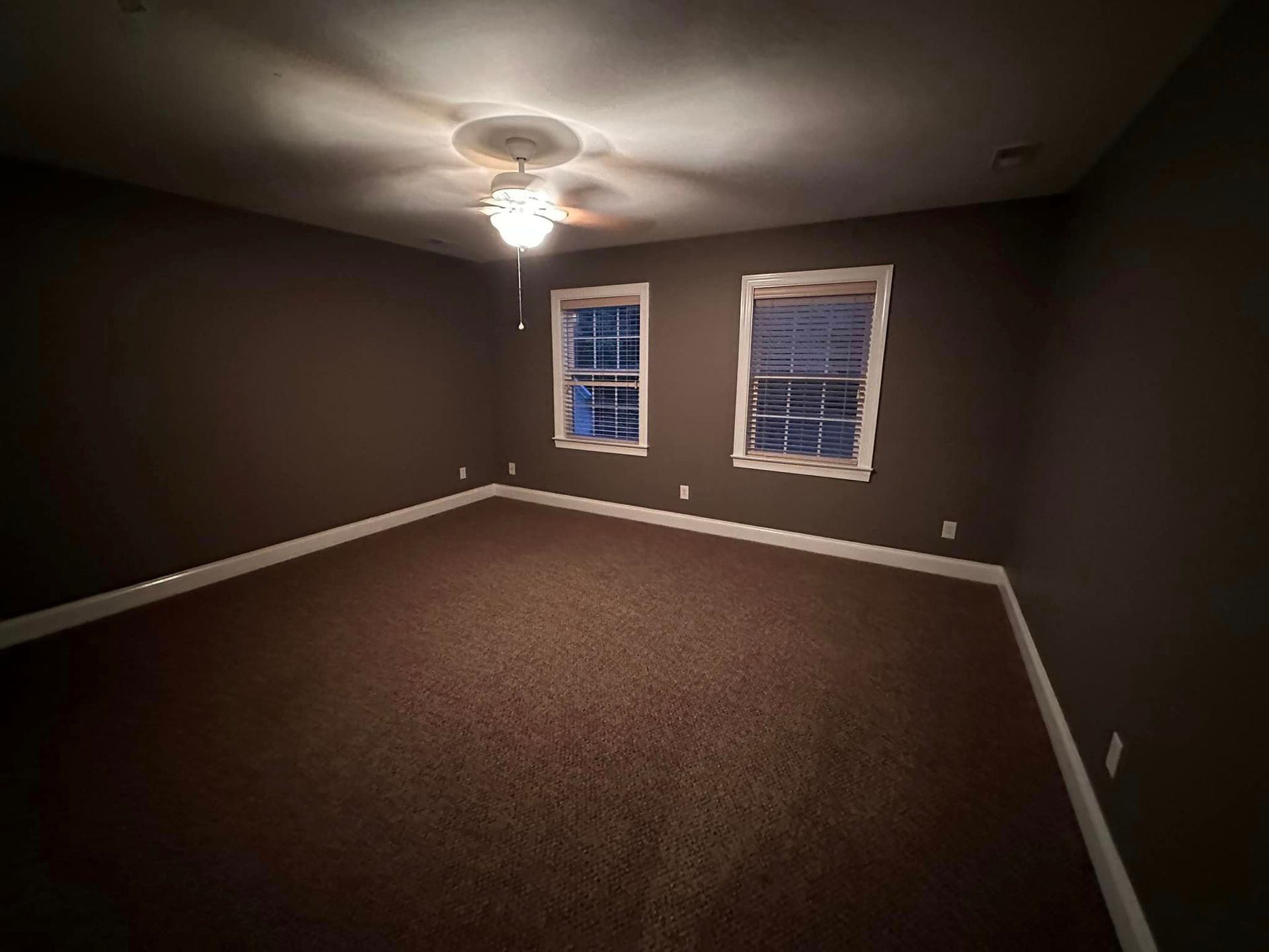 An empty room with two windows and a ceiling fan.