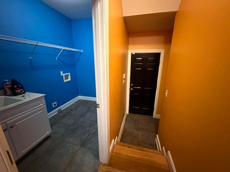 A laundry room with blue walls and orange walls and a black door.