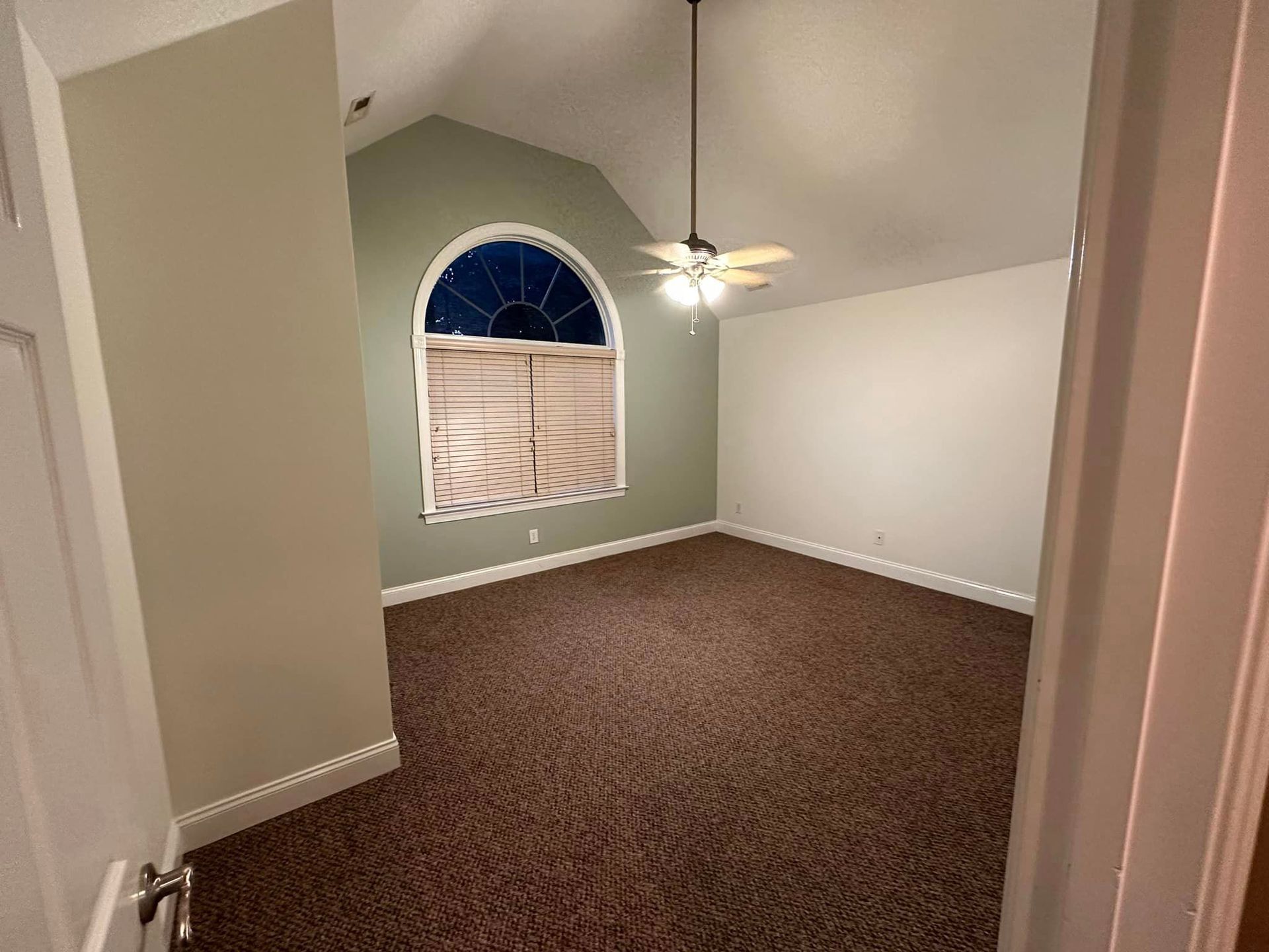An empty bedroom with a ceiling fan and a window.
