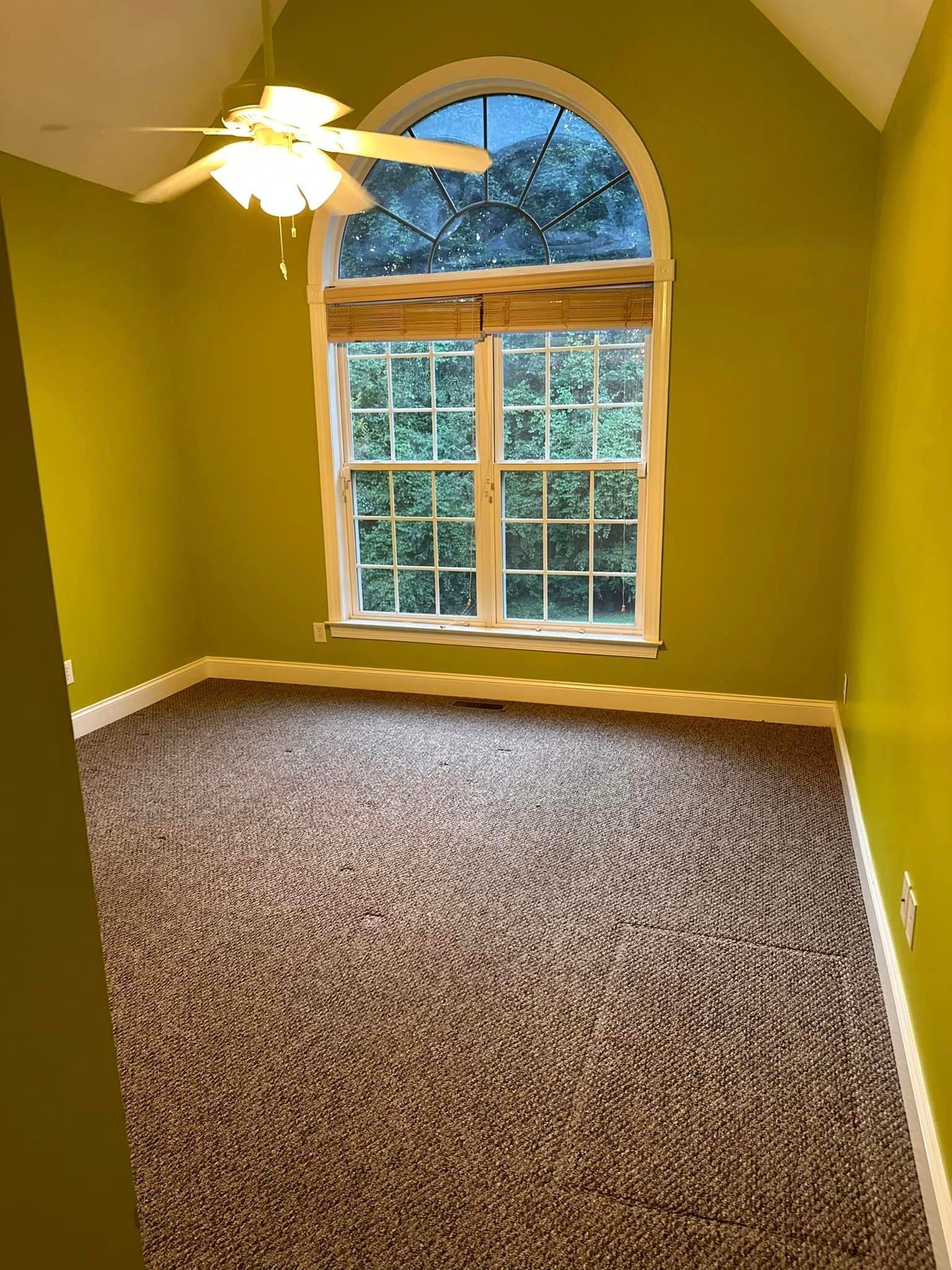 An empty room with a ceiling fan and a large window.