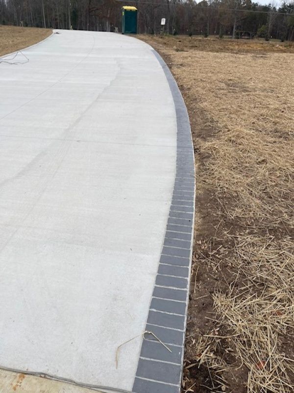 A concrete walkway with a tile border is going through a field.