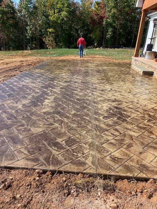 A man is standing on a concrete patio in a yard.