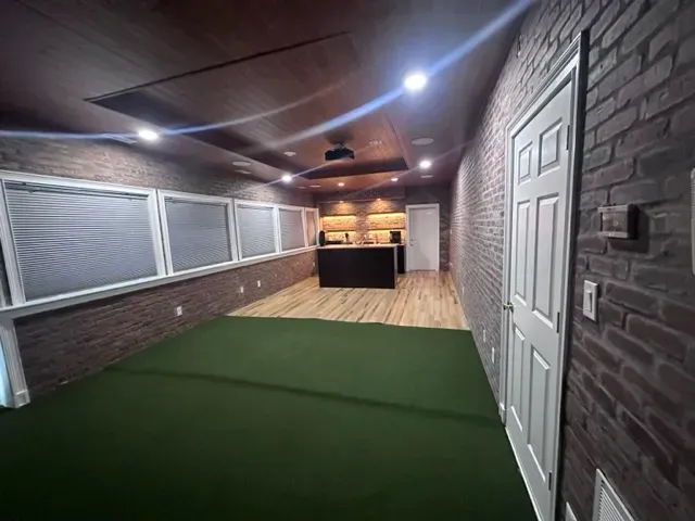 A long hallway with a green carpet and a brick wall.