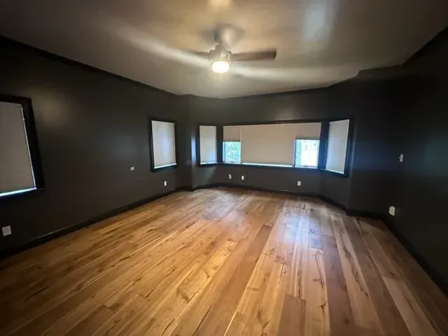 A large empty room with hardwood floors and a ceiling fan.