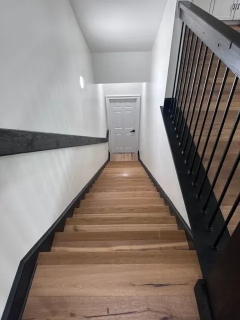 A wooden staircase with a black railing and a white door