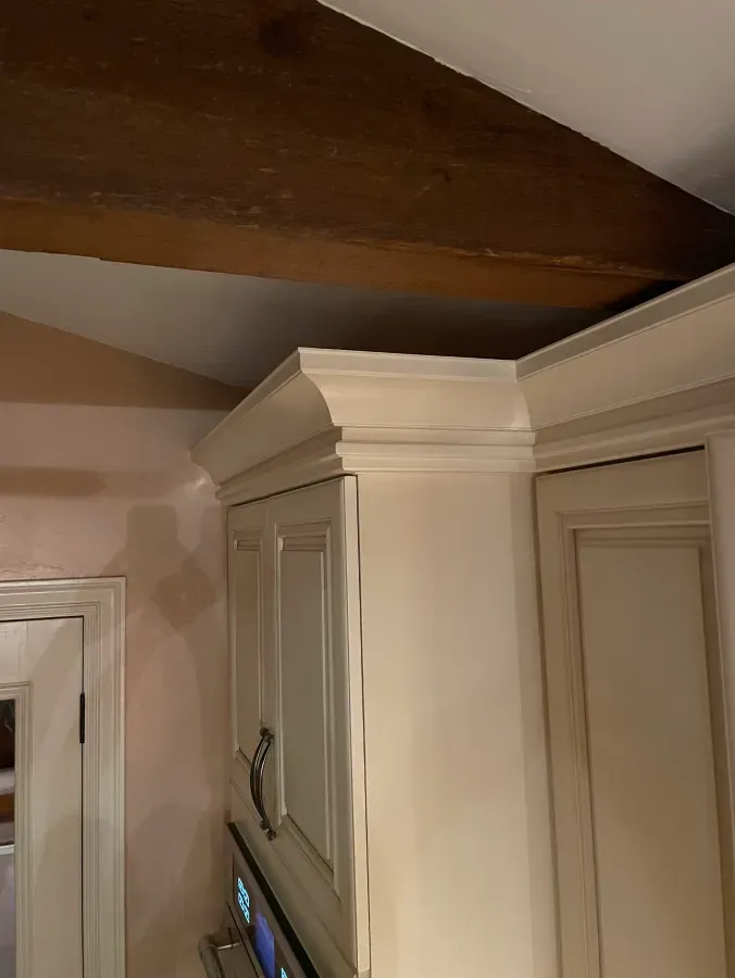 A kitchen with white cabinets and wooden beams on the ceiling.