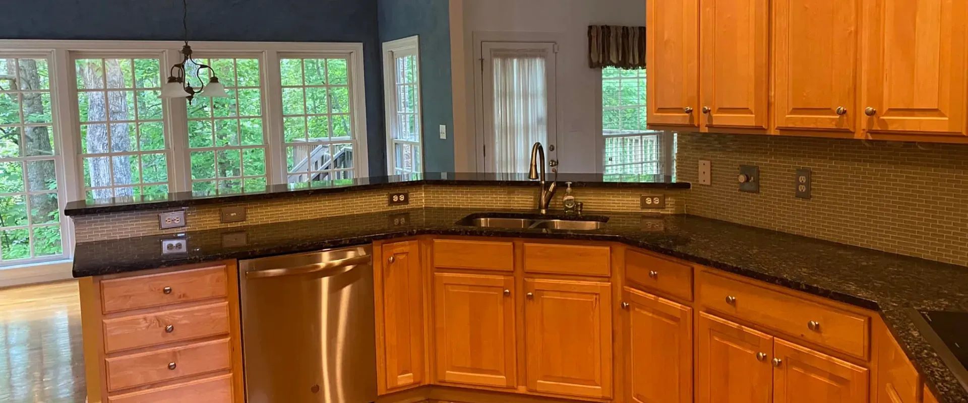 A kitchen with wooden cabinets , granite counter tops , stainless steel appliances and a large window.