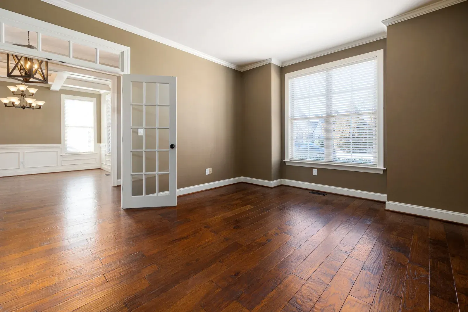 Empty room with brown hardwood floors, beige walls, a white-framed window, and a glass-paneled door.