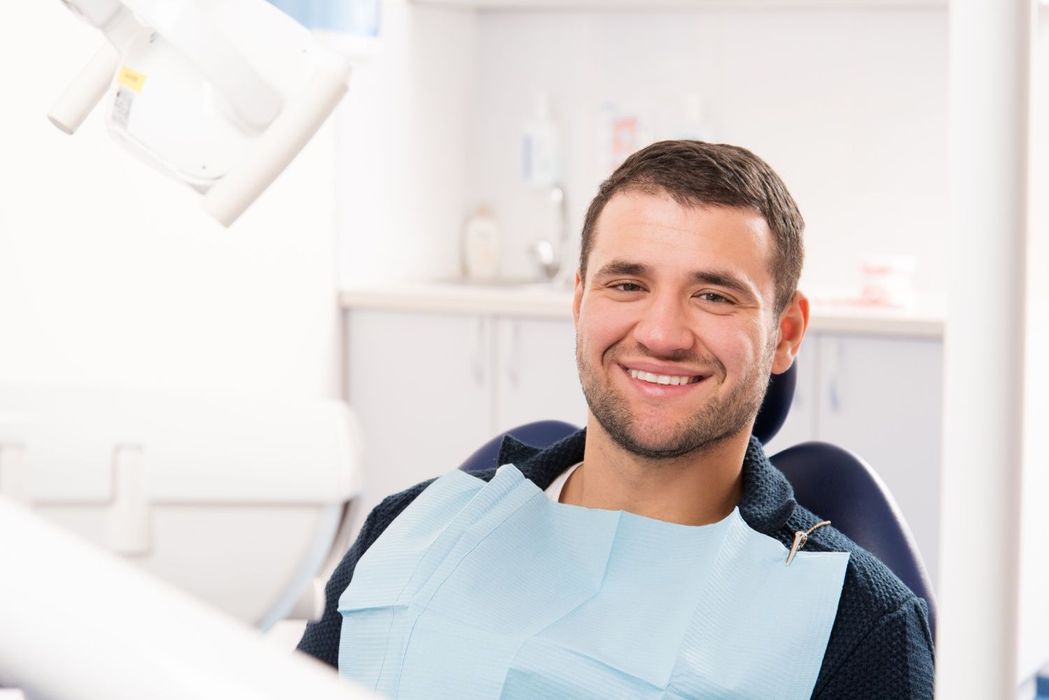 Man smiling in a dentist's chair with a bib on; dental office setting.